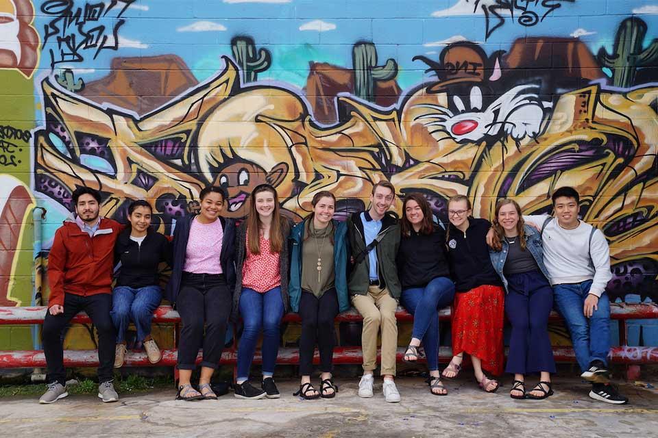 Immersion Program participants pose in front of a wall mural of cartoon character Sylvester the cat. 